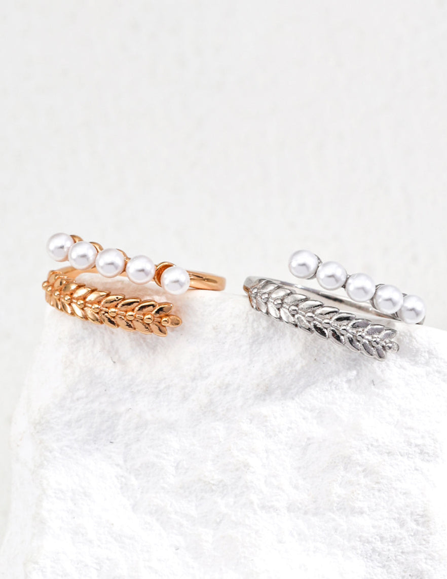 Two pearl-encrusted rings, one gold and one silver, on a white surface.