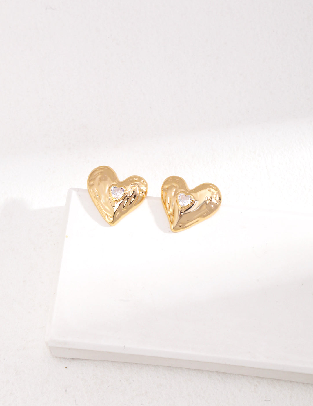 Gold heart-shaped earrings on a white surface