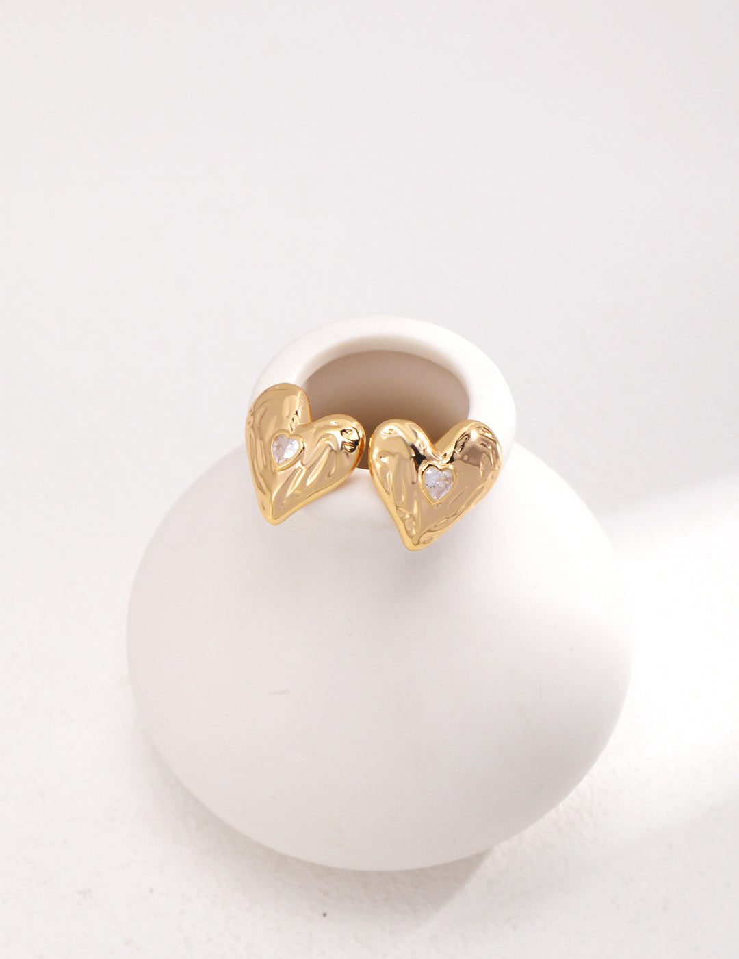 Gold heart-shaped earrings on a white spherical stand with a white background