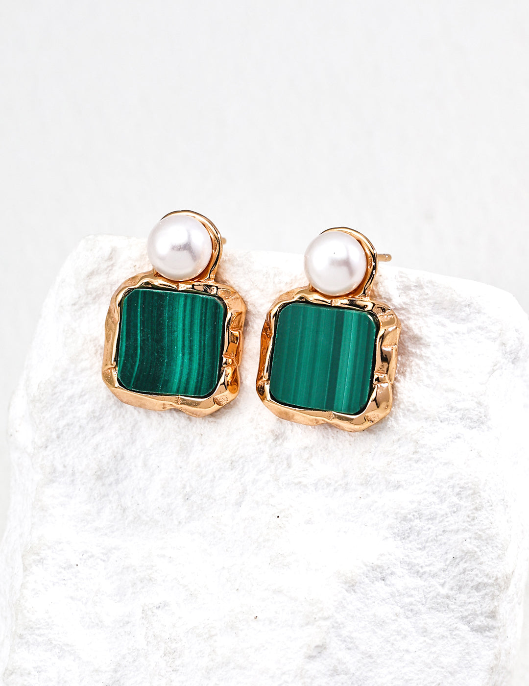 Pair of earrings with green square stones and pearl-like centers on a white fabric background