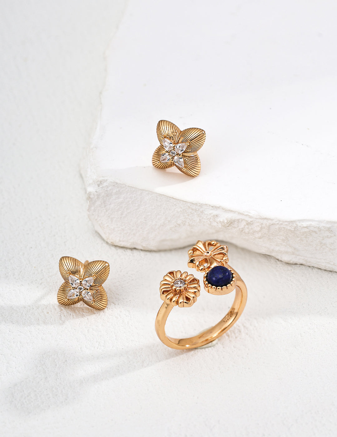 Gold floral earrings with gemstones on a white fabric background