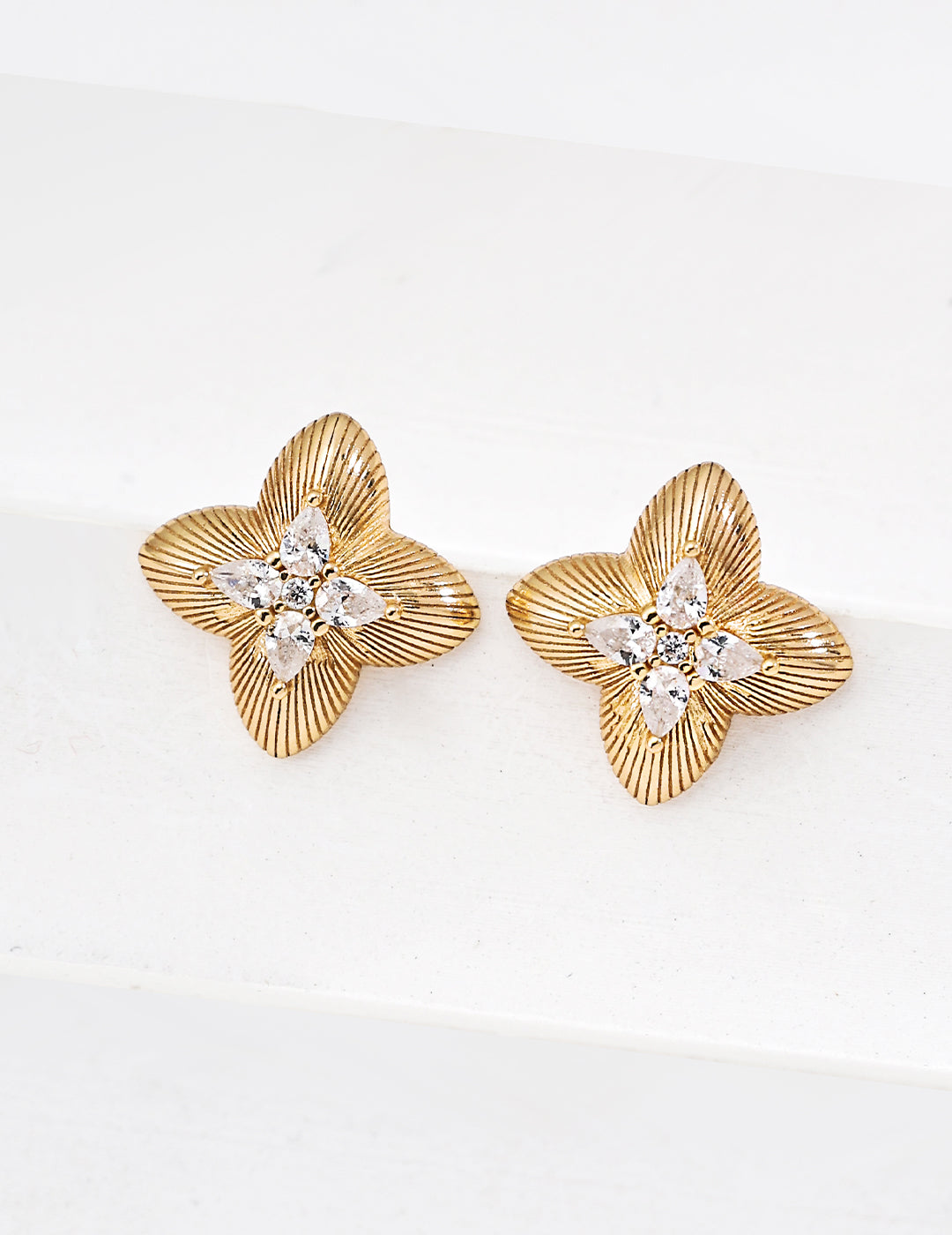 Gold floral earrings with diamond-like centers on a white background