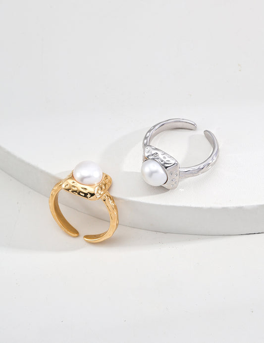 Two pearl rings, one gold and one silver, on a white surface.