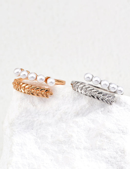 Two pearl-encrusted rings, one gold and one silver, on a white surface.