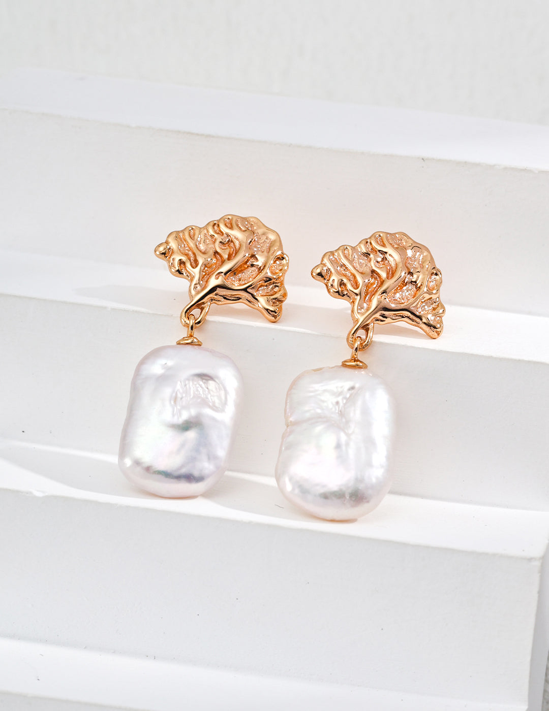 Gold earrings with baroque pearl drops on a white background